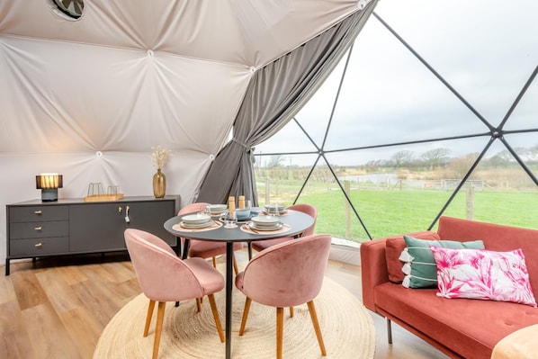 A tented accommodation with a dining table, chairs, a sofa, and a cabinet.