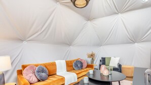Et værelse med en polstret sofa, et rundt bord og en hængende lampe.