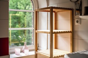 Ein Zimmer mit einer Holzregaleinheit, einem Fenster mit Blick ins Grüne und einer Blumenvase auf der Fensterbank.