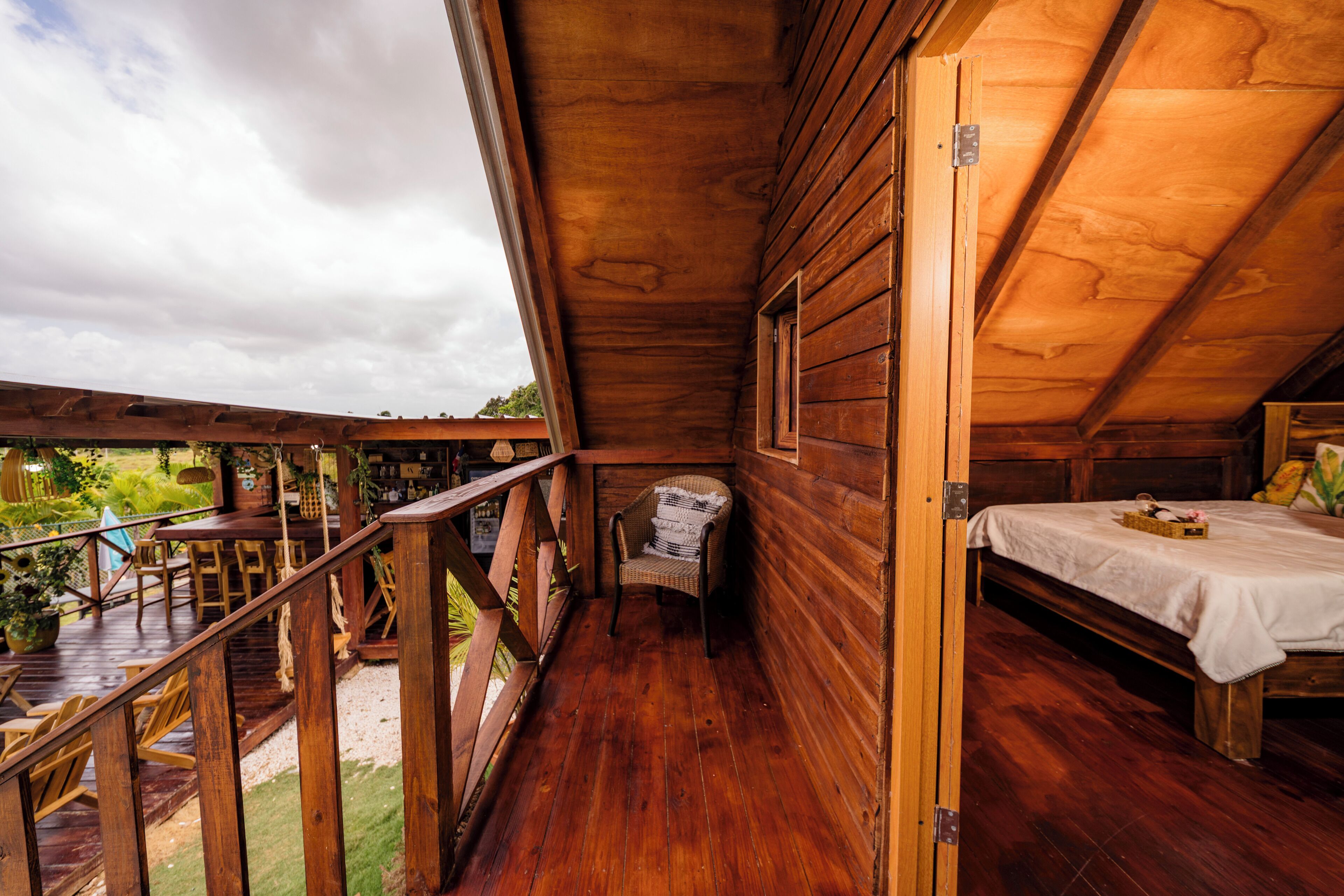 Una baita di legno con un balcone, un letto e una sedia in vimini.
