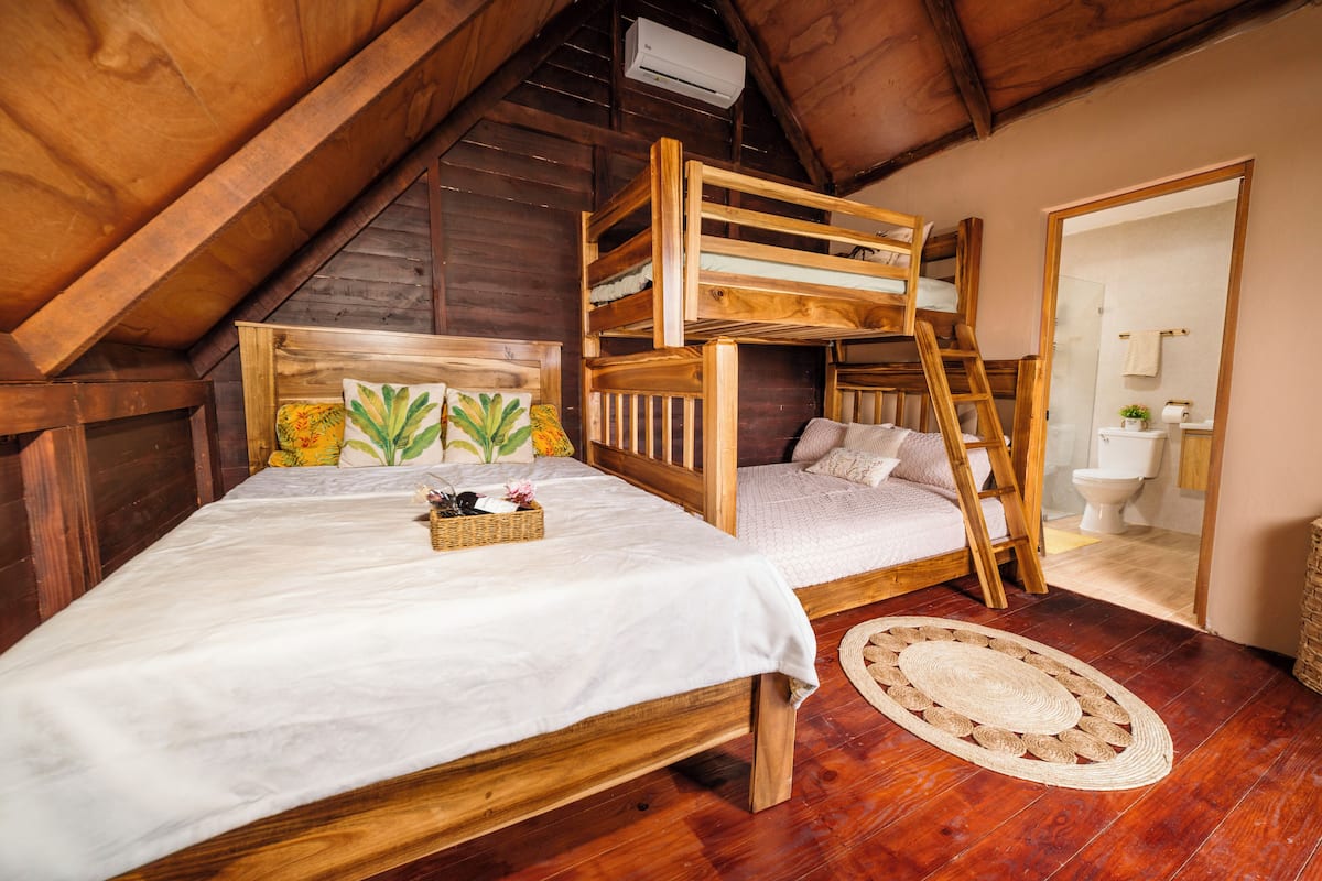 Un lit superposé en bois avec une échelle, une table de chevet avec un panier et un tapis tissé.