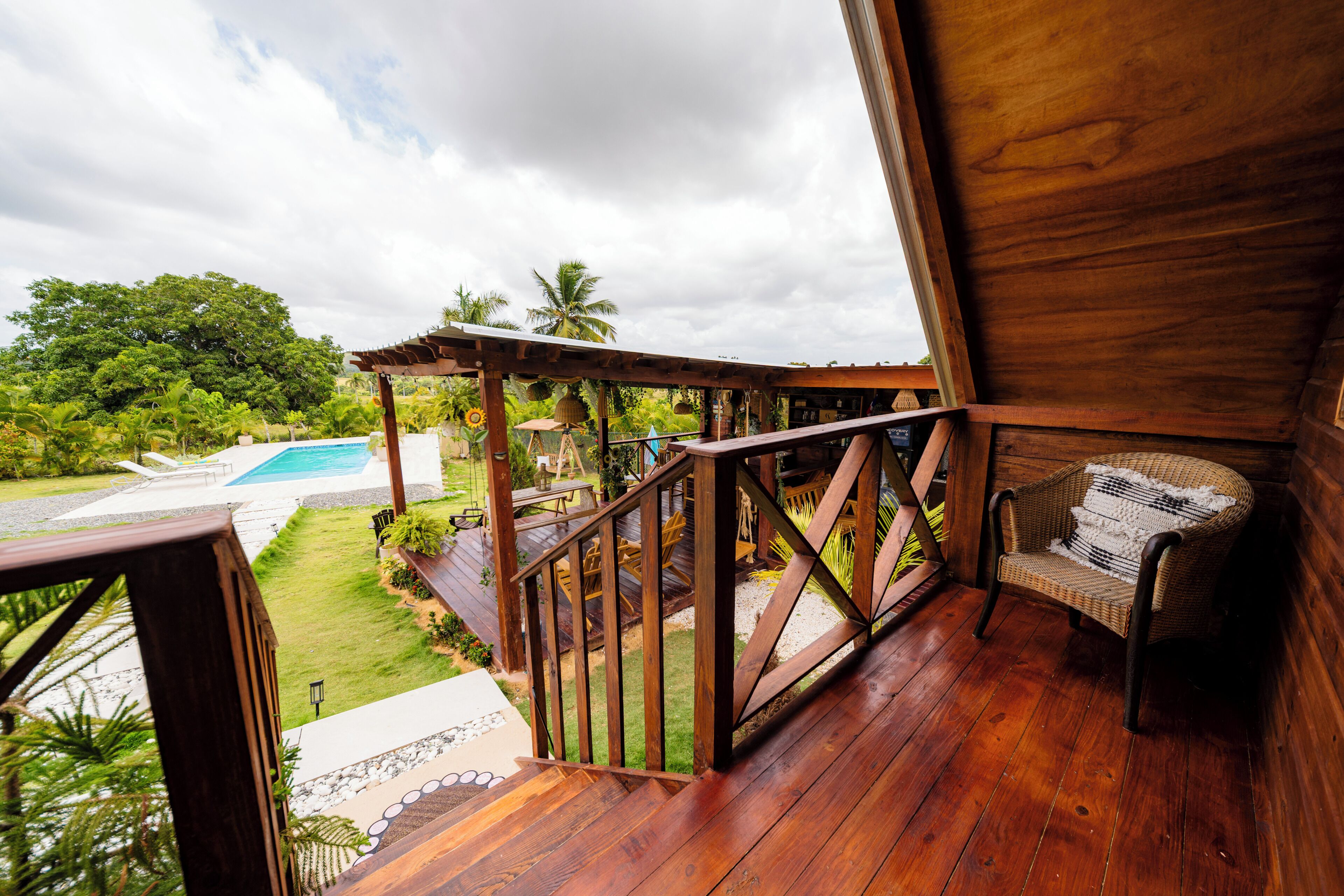 A wooden deck with a view of a swimming pool and lush greenery.