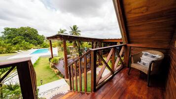 A wooden deck with a view of a swimming pool and lush greenery.