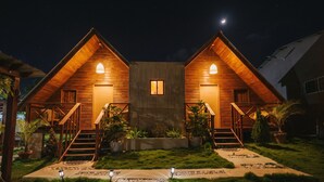 A two-story wooden cabin with a central window, surrounded by a well-maintained lawn and potted plants. - Villa Campestre by Otium (Higüey)
