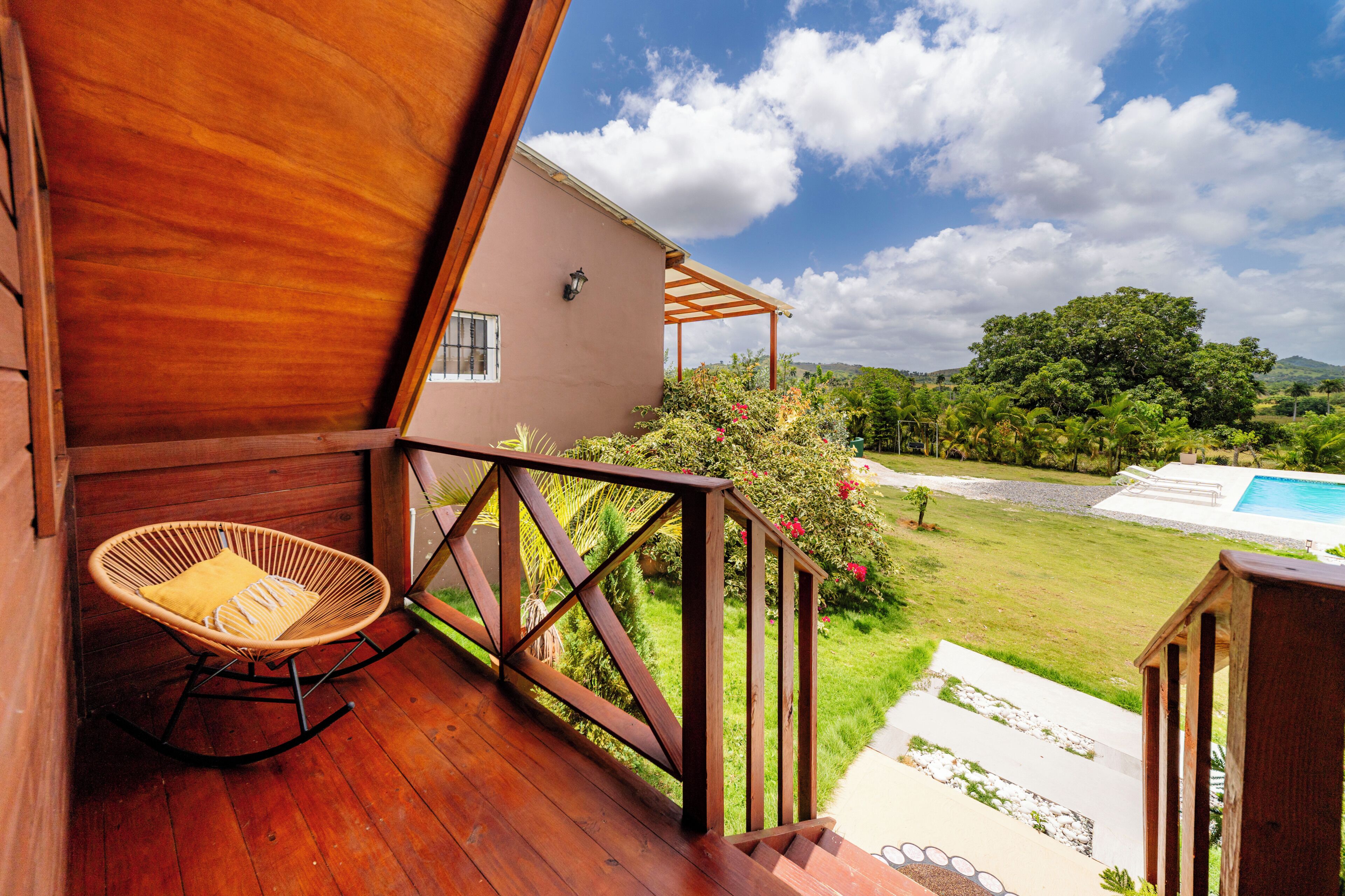 A wooden deck with a rocking chair, a pool, and a view of a green landscape.