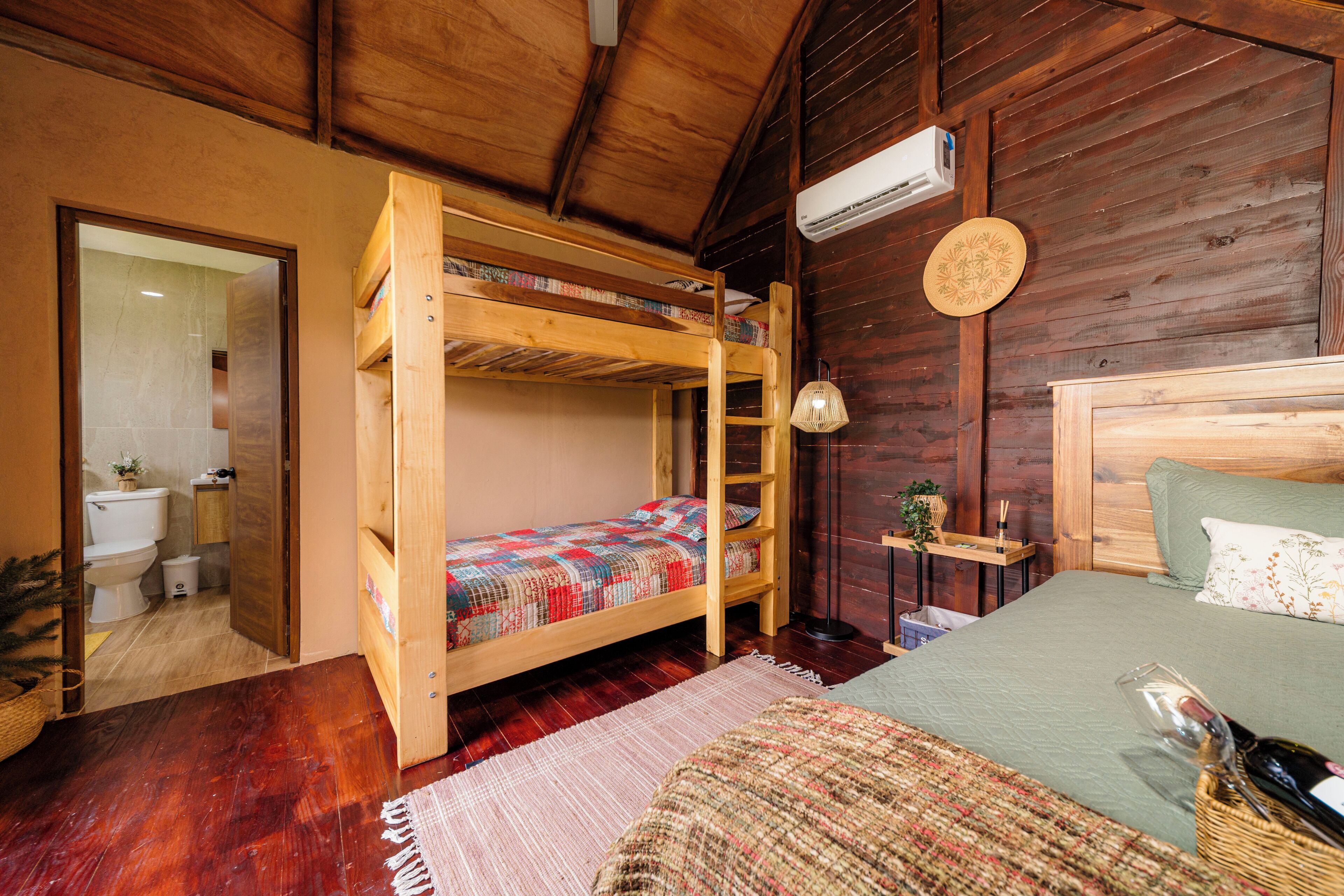 A wooden bunk bed with a ladder, a single bed with a green bedspread, a round wall clock, and a small shelf with a plant.