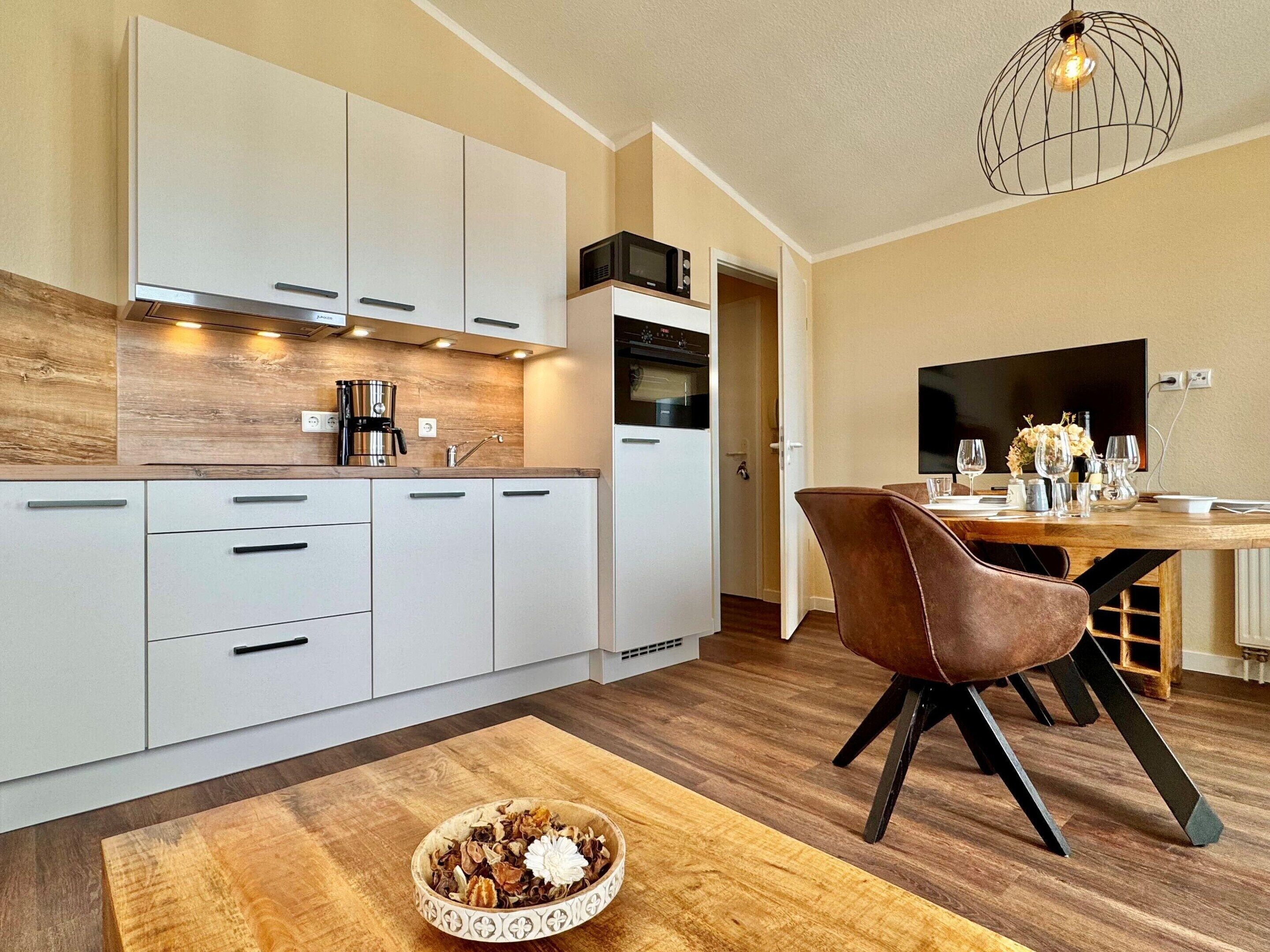 Una cucina moderna con mobili bianchi, un piano di lavoro in legno e una zona pranzo con una sedia e un tavolo marroni.