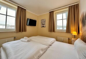 Ein Hotelzimmer mit zwei Betten, einem Fernseher, einem Gemälde und Blick ins Freie.
