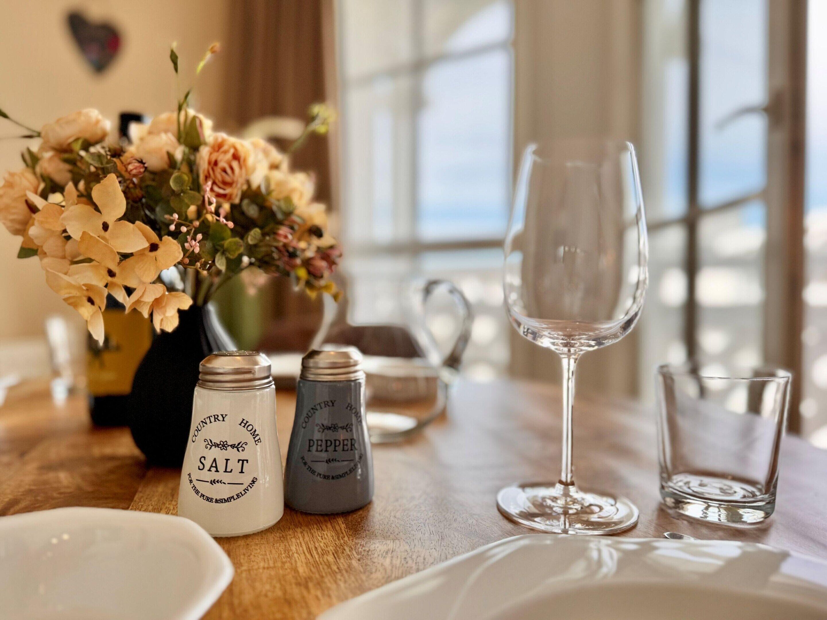 A dining table with a vase of flowers, salt and pepper shakers, a wine glass, and a glass of water.