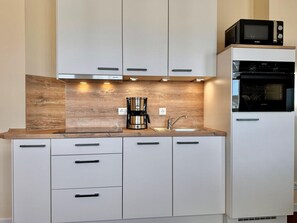 A kitchen with white cabinets, a wooden countertop, a coffee maker, a sink, and a microwave. - Stilvolle Ferienwohnung mit Balkon und Wlan in Sellin (Sellin)