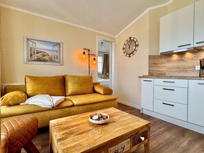 Ein Wohnzimmer mit einer Couch, einem Holztisch und einer Küchenzeile mit Schränken.