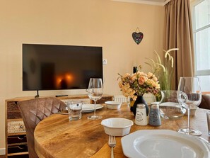 Ein Esstisch mit Fernseher, Weingläsern, einer Blumenvase, Salz- und Pfefferstreuern sowie einer herzförmigen Dekoration an der Wand.