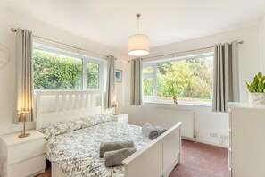 Ein Schlafzimmer mit einem Bett, Nachttischen, einem Heizkörper und einem Fenster mit Vorhängen.