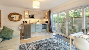 A modern kitchen with a microwave, oven, and sink, a dining area with a table and chairs, and a large sliding glass door to a garden. - 1 Bed in Exmouth (oc-c33052) (Exmouth)