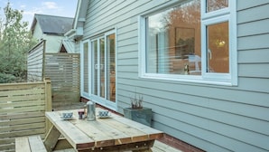 A wooden deck with a table, a window with a view of a tree, and a fence. - 1 Bed in Exmouth (oc-c33052) (Exmouth)