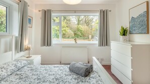 A bedroom with a bed, a radiator, a window with curtains, a bedside table with a lamp, a dresser, and a framed picture on the wall. - 1 Bed in Exmouth (oc-c33052) (Exmouth)
