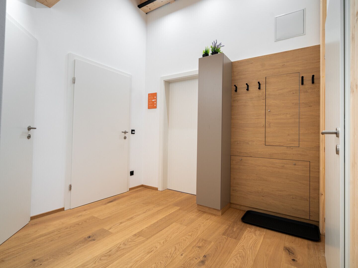Un pasillo con suelo de madera, paredes blancas y una puerta de madera con picaporte negro.