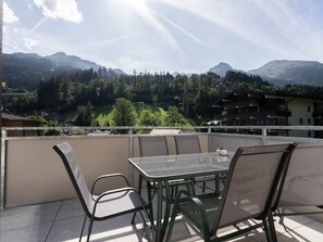 Ein Balkon mit Tisch und Stühlen, der auf eine gebirgige Landschaft mit Gebäuden in der Ferne blickt.