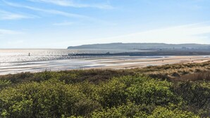 Un paysage côtier avec une plage, des dunes herbeuses et une colline qui se dessine à l’horizon.