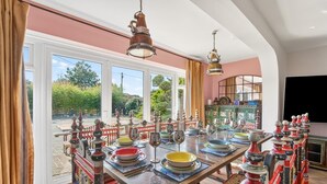 Un espace repas avec une grande table dressée pour le repas, une vue sur l’extérieur et une collection d’objets décoratifs accrochés aux murs.