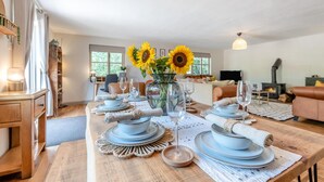 Een eetgedeelte met een houten tafel gedekt voor vier personen, een vaas met zonnebloemen en een open haard op de achtergrond.