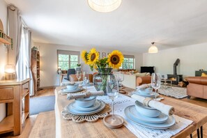 Ein Essbereich mit einem Holztisch, gedeckt für vier Personen, einer Vase mit Sonnenblumen und einem Kamin im Hintergrund.