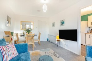 A living room with a sofa, a coffee table, a TV, and a dining area with a table and chairs.