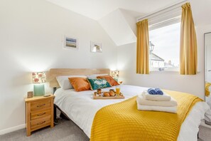 A bedroom with a bed, bedside tables, a window with curtains, and a view of buildings outside.