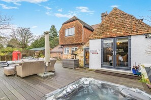 A wooden deck with outdoor furniture, a hot tub, and a brick house with a window. - 4 Bed in Burwash Common (oc-b34866) (Burwash)