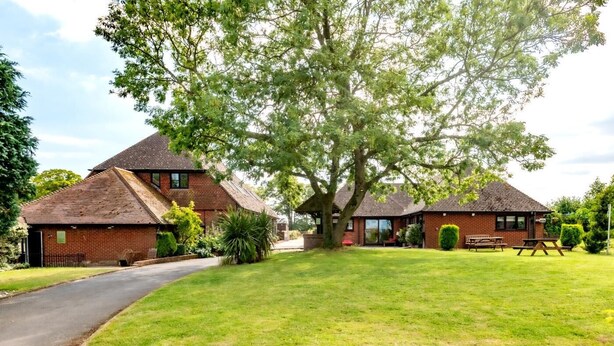 A two-story brick building with a sloped roof, a paved driveway, and a well-maintained lawn. - 2 Bed in Alkham (oc-p34786) (Swingfield)