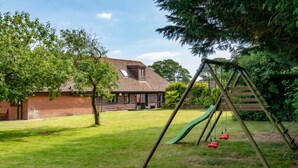 A backyard with a swing set, a brick house, and a lawn. - 2 Bed in Alkham (oc-p34786) (Swingfield)