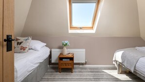 Une chambre avec un plafond en pente, un puits de lumière, un radiateur, une table de chevet avec un vase et deux lits.