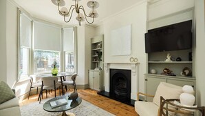Een woonkamer met een open haard, een televisie en een eethoek met stoelen en een tafel.