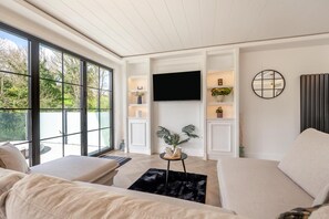 A modern living room with a large window, a flat-screen TV, and built-in shelving with decorative items.