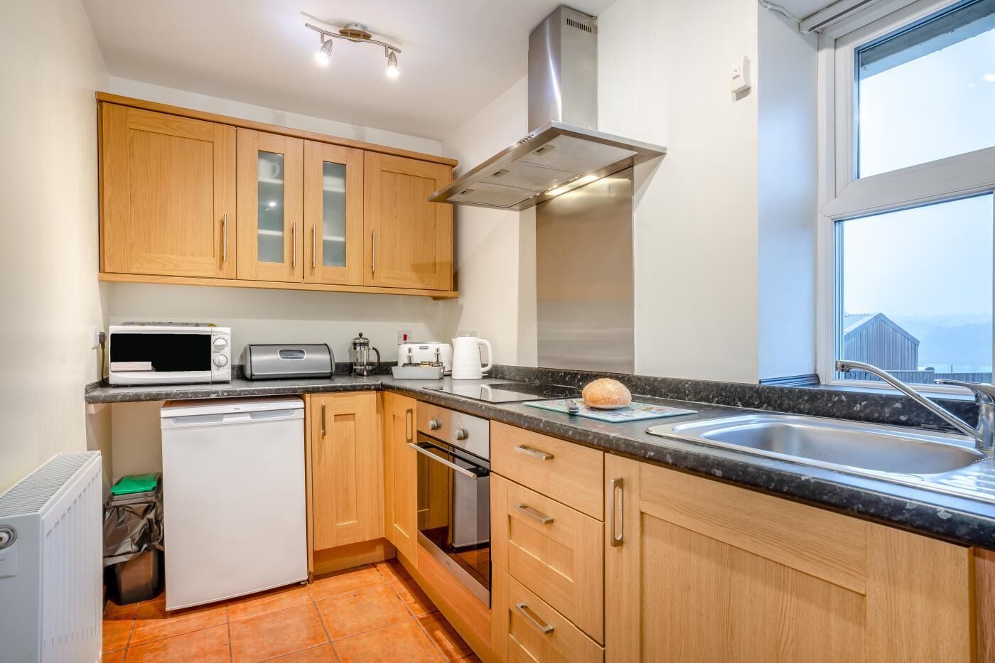 A compact kitchen with wooden cabinets, a microwave, toaster, kettle, and a sink.