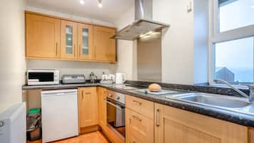 A compact kitchen with wooden cabinets, a microwave, toaster, kettle, and a sink.