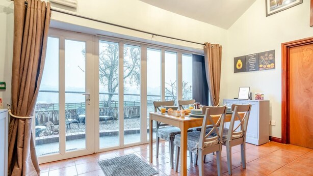 Comedor con una mesa dispuesta para dos, vista a través de amplios ventanales y zona de cocina con encimera y armarios.