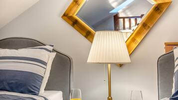 A hotel room with a bed, a bedside table with a lamp, two glasses of orange juice, and a large mirror on the wall.