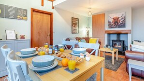 Comedor con mesa de madera dispuesta para el desayuno, chimenea y una escalera estilo loft.