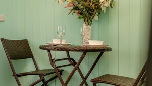 Een kamer met een lichtgroene wand, een kleine ronde tafel met een glazen vaas en een wijnglas, en twee rieten stoelen.