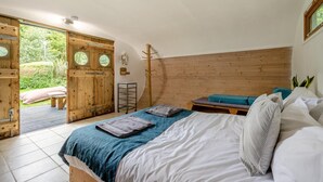 A bedroom with a bed, a bench, and a wooden door leading to a garden. - 1 Bed in Bude (oc-s34860) (Bude)