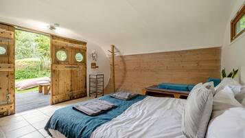 A bedroom with a bed, a bench, and a wooden door leading to a garden.