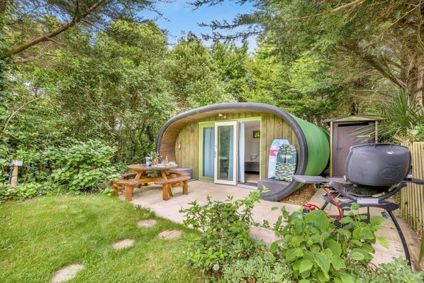 Un espacio al aire libre acogedor con una estructura de madera curvada, una parrilla y una mesa de picnic.