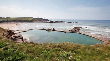 A coastal landscape with a clear pool, beach, and rocky outcrops.
