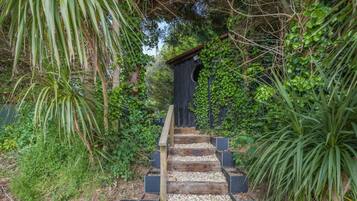 A wooden staircase with black steps leading up to a dark wooden structure surrounded by dense greenery.