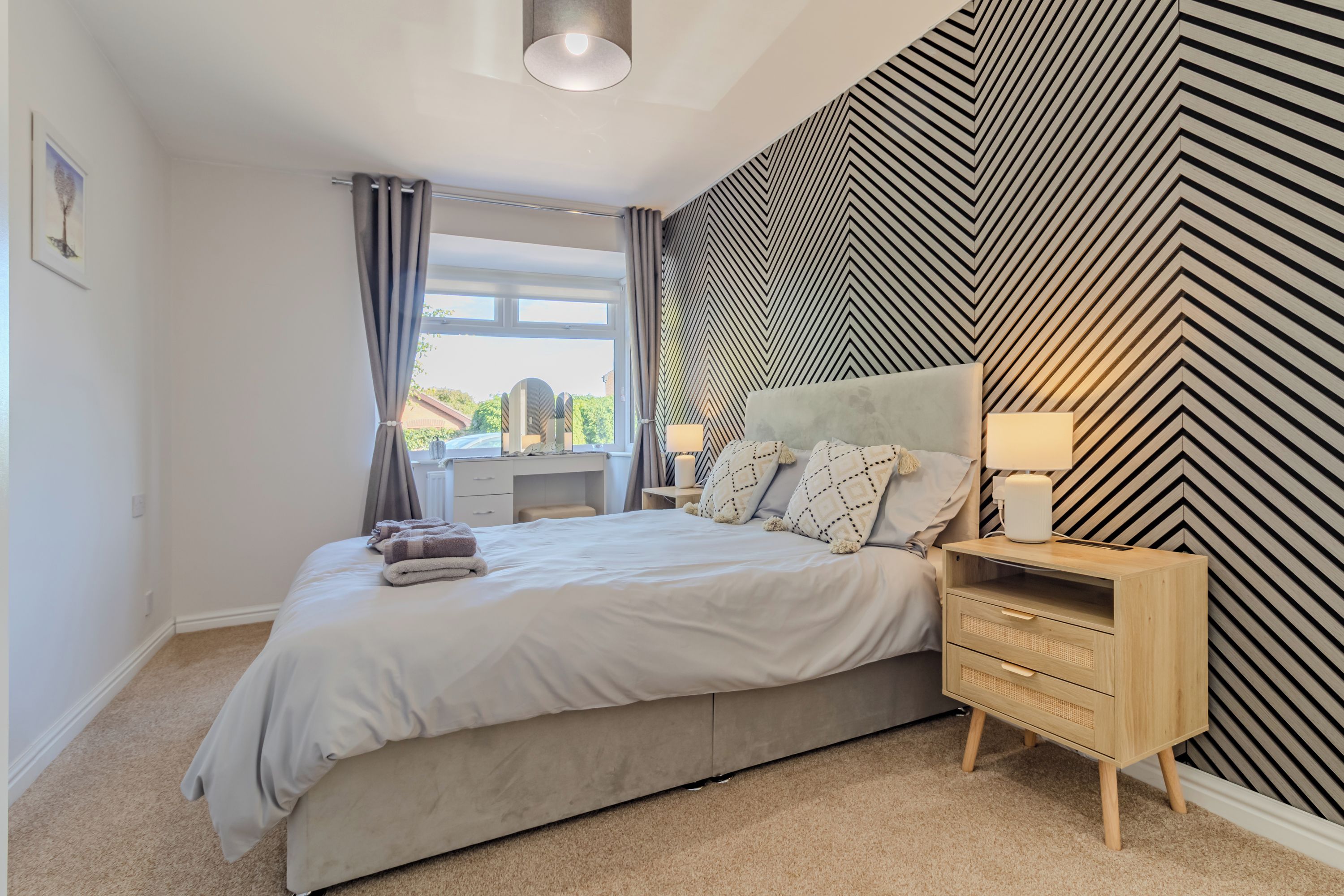 A bedroom with a bed, bedside table, lamp, and a wall with a geometric pattern.