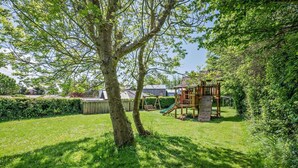 A backyard with a wooden play structure, a tree, and a grassy lawn. - 1 Bed in Bude (oc-s34854) (Bude)