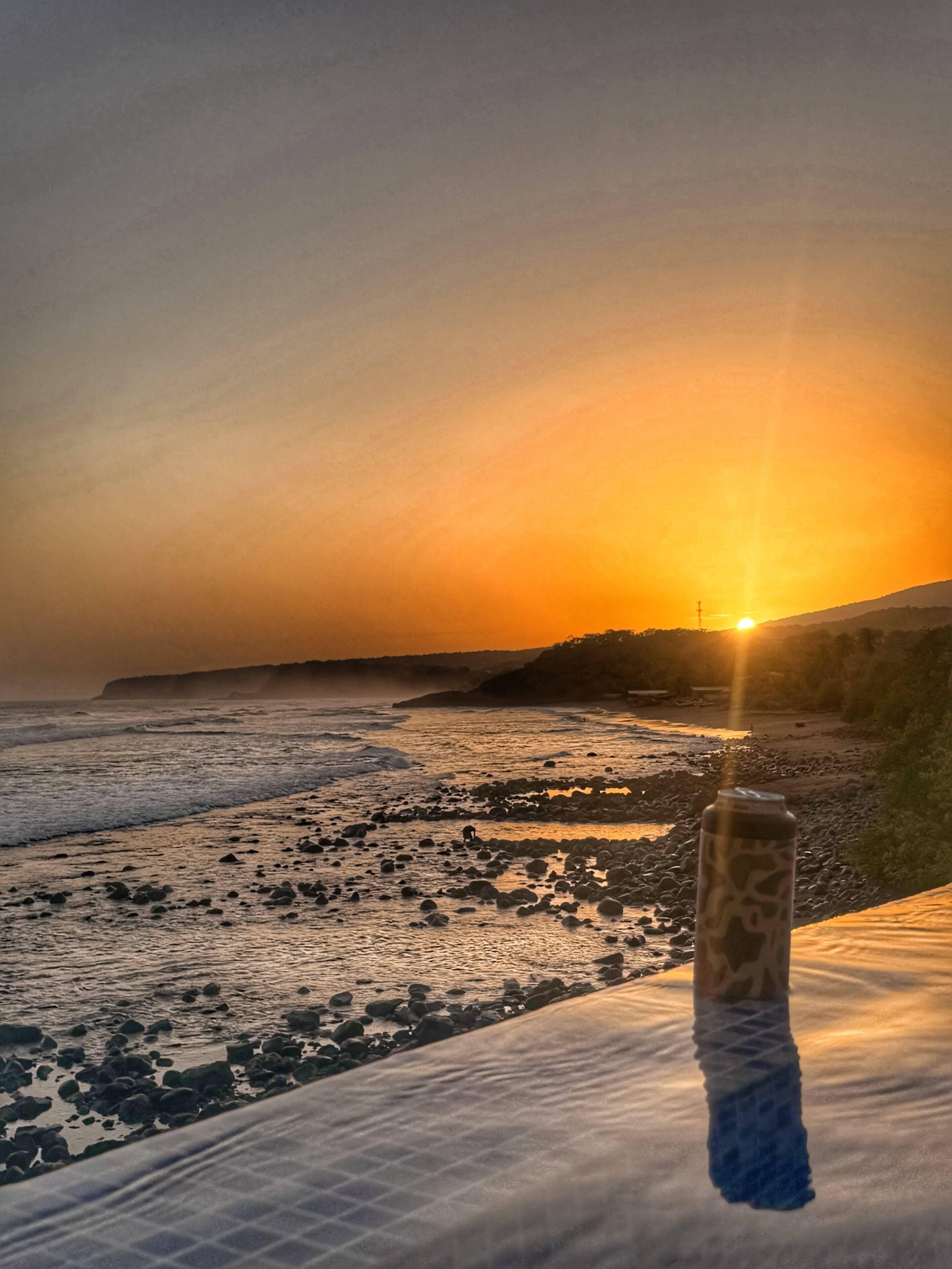 A sunset over a beach with a bottle in the foreground.