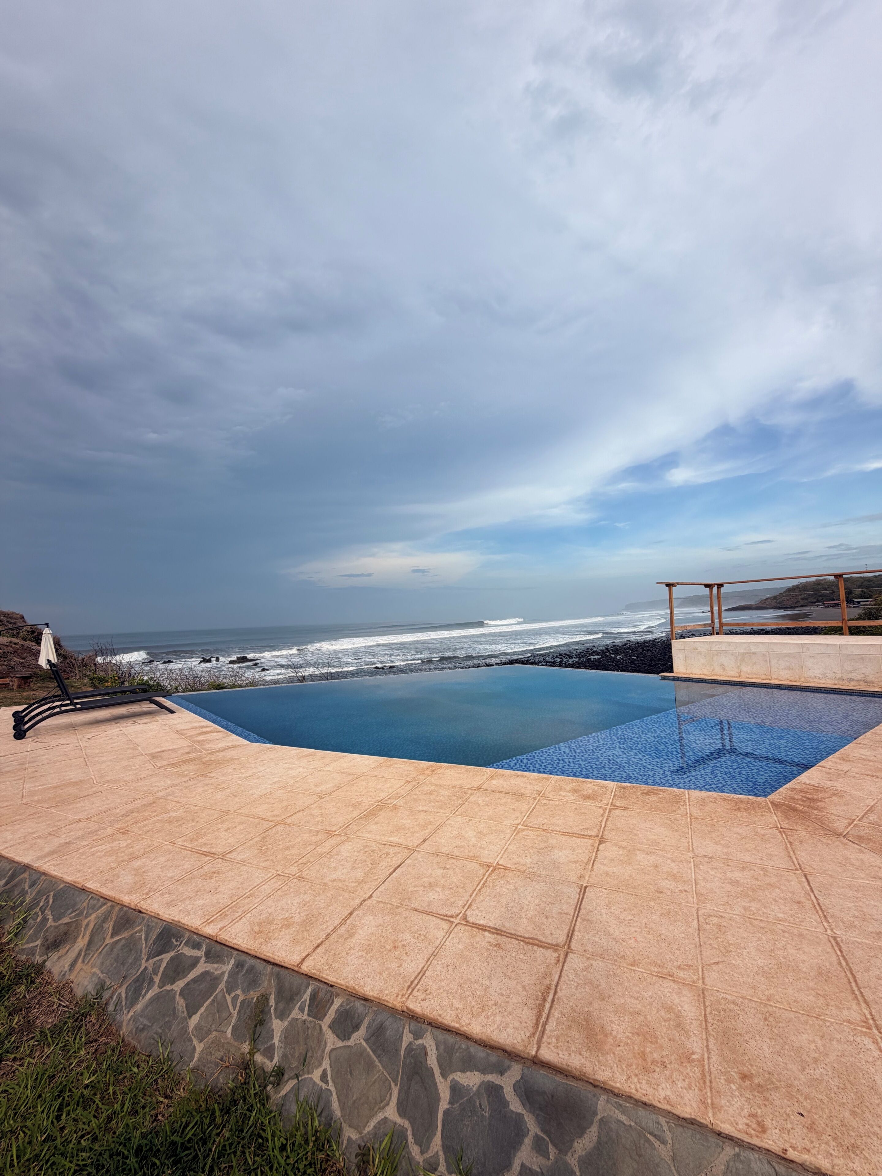 Una piscina con vistas al océano, una silla de descanso y un patio con baldosas de piedra.