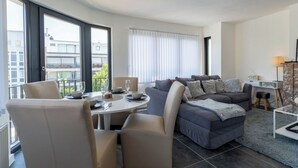 Ein modernes Wohnzimmer mit Essbereich, großen Fenstern und Blick auf Gebäude.